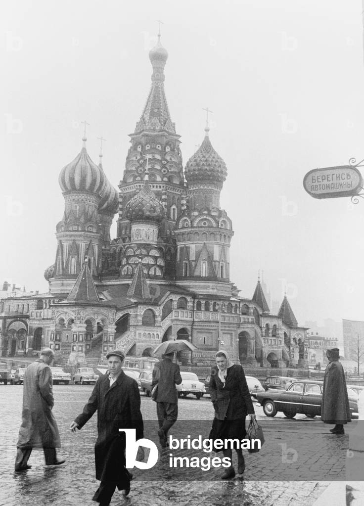 Moscovites with their heads down against the rain seen here passing St Basil's Cathedral in Red Square. April 1960