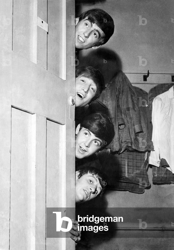 The Beatles peering out from behind their dressing room door before their appearance at the Odeon Theatre in Manchester. Top to bottom: George Harrison, John Lennon, Paul McCartney and Ringo Starr. 30th May 1963 (b/w photo)
