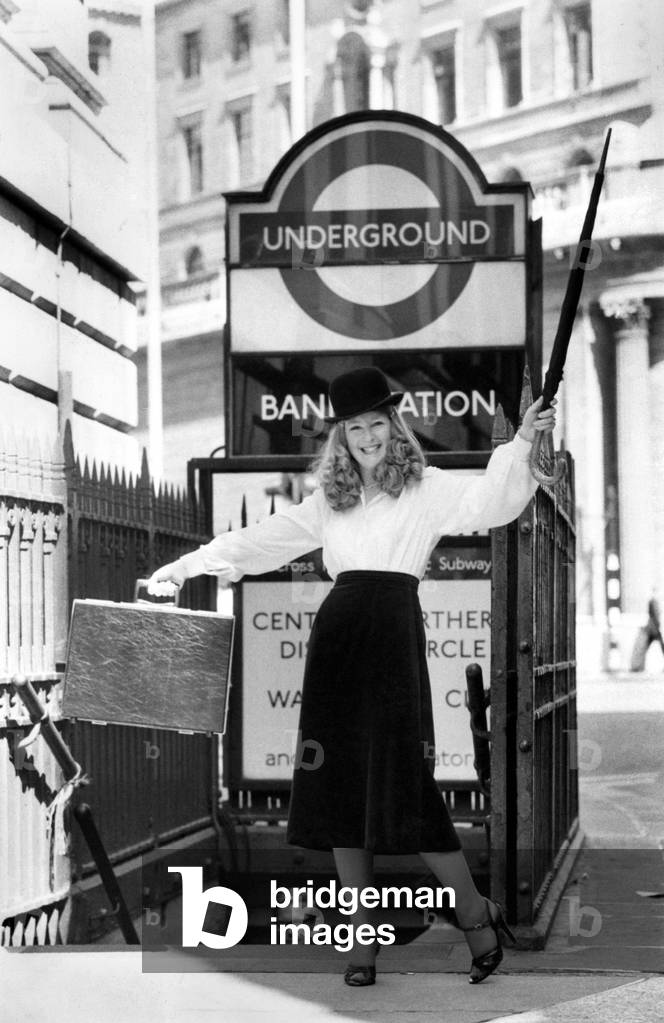 Top Secretary of 1978, Andrea Mullancy wearing a bowler hat and holding an umbrella outside a London tube station, August 1978 (b/w photo)