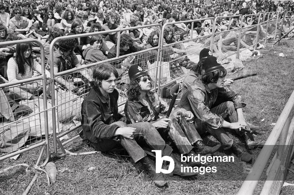 Reading Pop Festival. Music fans wearing police helmets and holding truncheons watch the bands performing on the main stage, 26th June 1971 (b/w photo)