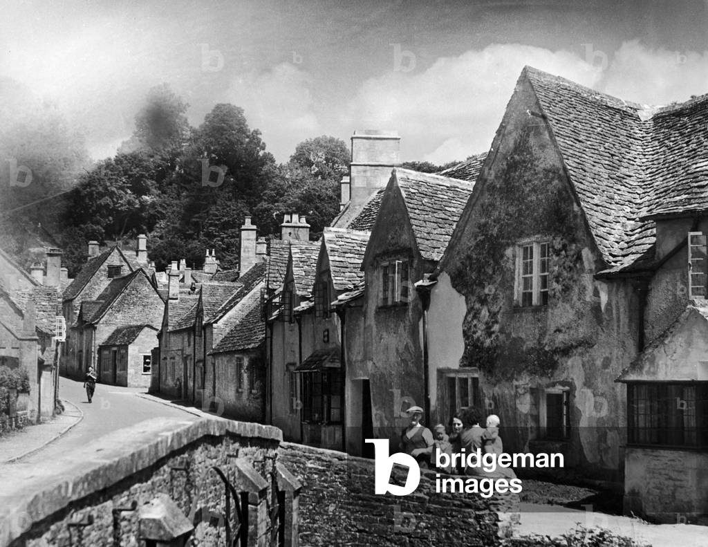 A family takes a rest on a stone wall in a Cotswold village in Gloucestershire, c. 1935 (b/w photo)