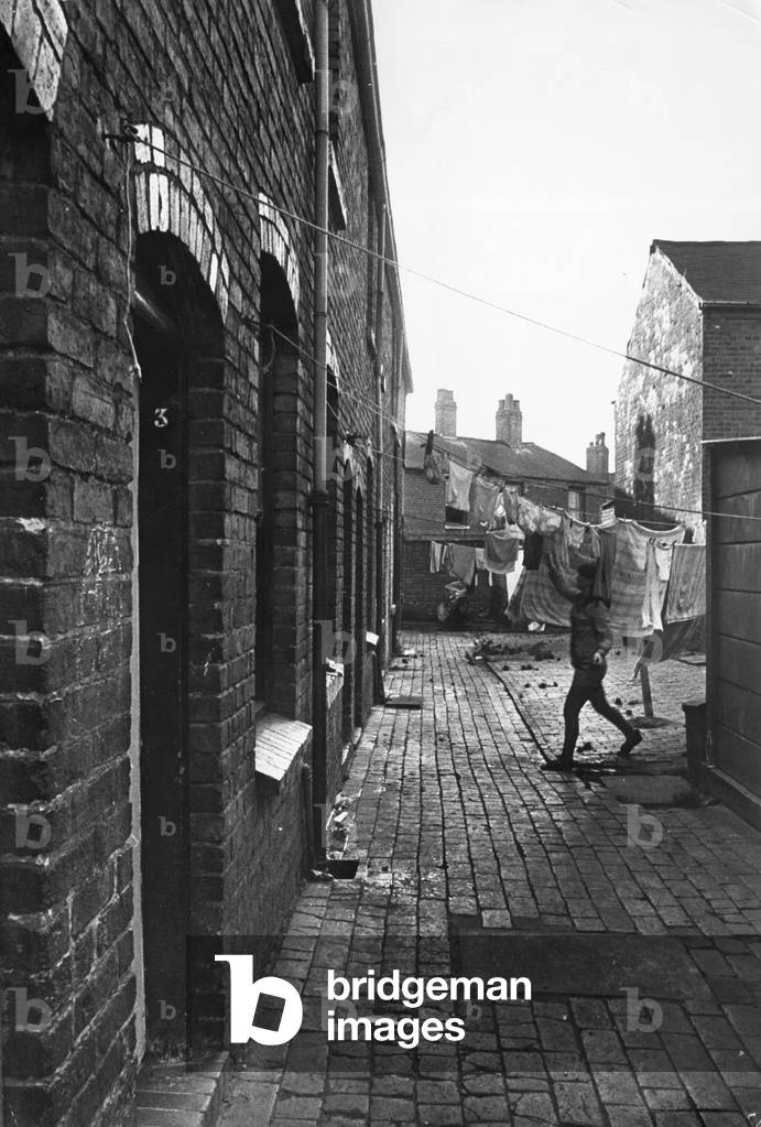 Exterior view of a Birmingham terraced house showing a woman hanging out her laundry
November 1971