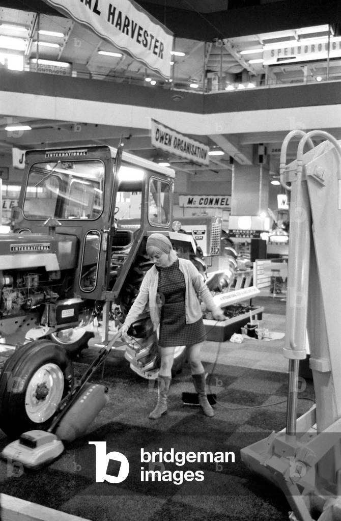 Exhibits are put in place at Earls Court for the Royal Smithfield Show. There are two sections, one for the machinery where everything is spick and span and cleaners going to and fro. In the other section amongst farm yard atmoshpere and slightly slippery underfoot are the animals.Mrs. Josephine Brandon hoovering round some heavy machinery. December 1969