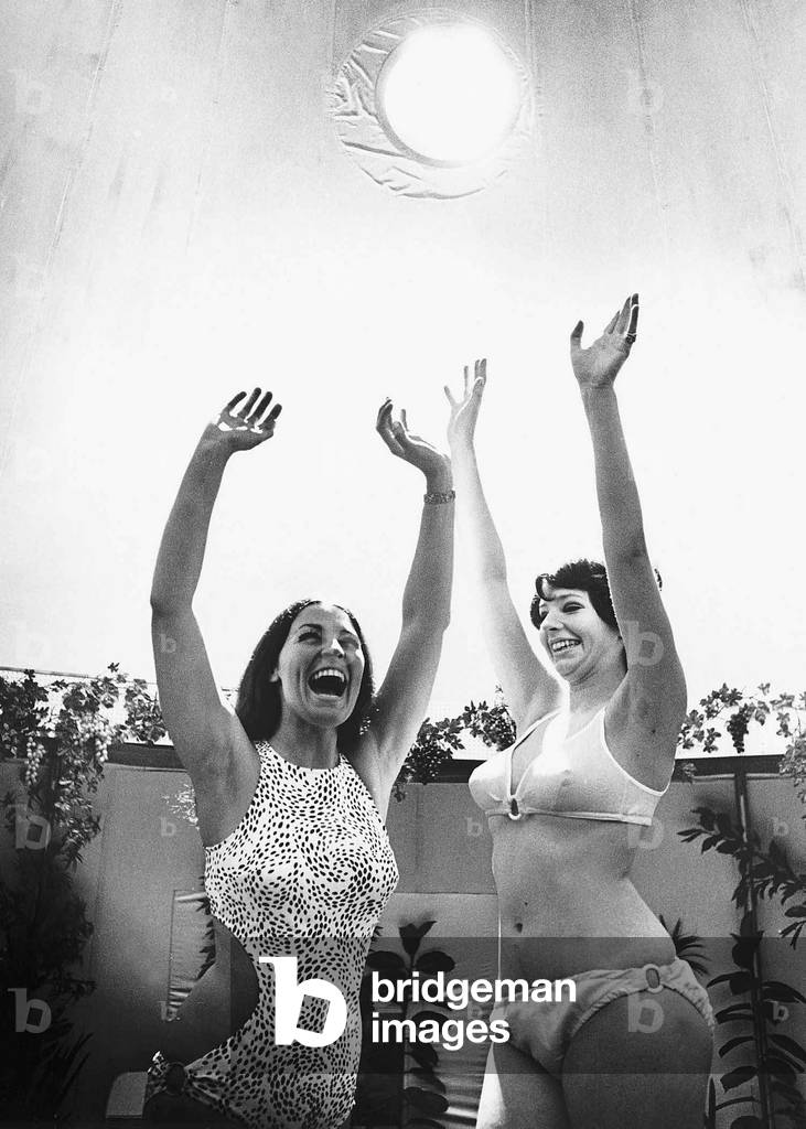 Miss Great Britain (L) and Actress Trix Pelham revel in the artifical sunshine of the solarium both with their arms in the air. 1968