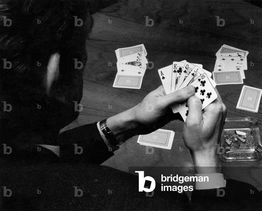 A man holding his hand of cards, a royal flush, while playing poker. 
February 1972
