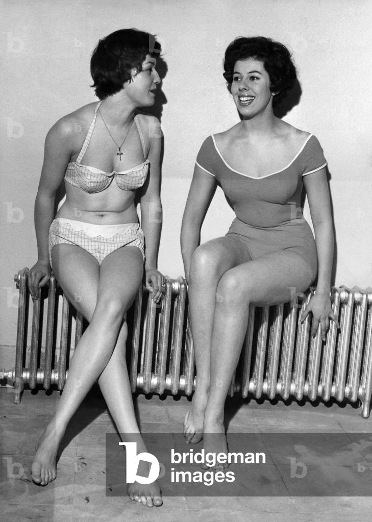 Strip Freeze. Models Verna Clarke and Thelma Drabble were happy to find this warm spot yesterday (14-1-59) at London's White House swimming pool. While everyone else was wrapping up against the icy weather Verna and Thelma had to strip off to parade at a swimsuit fashion show. Verena's bikini is in printed cotton lastex with a built - in bra and Thelma's is in cotton poplin. January 1959