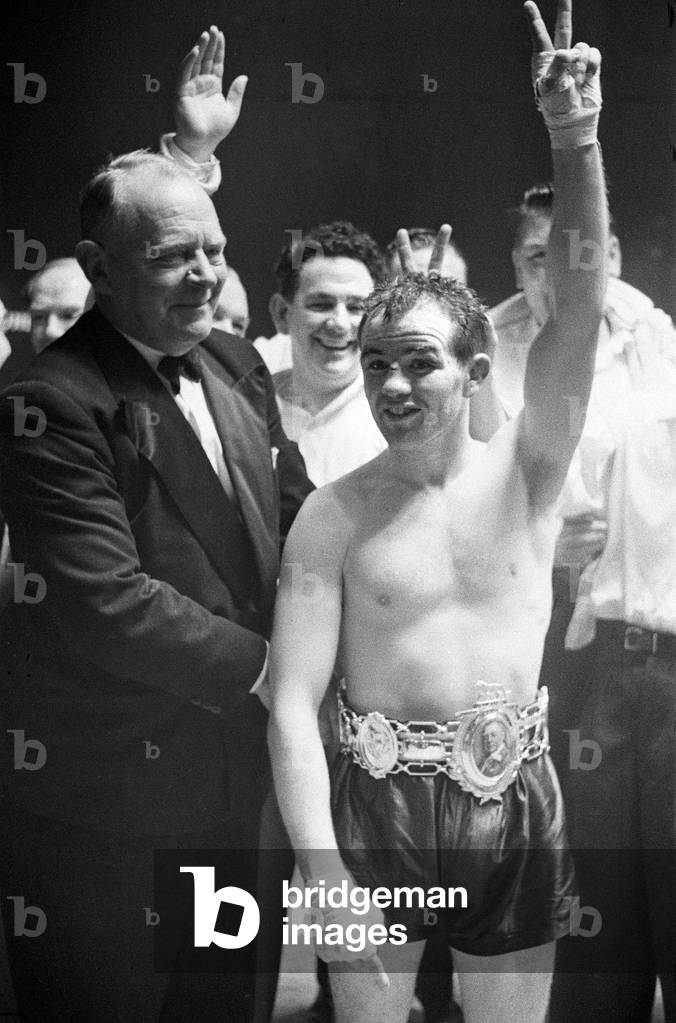 BBBofC British bantamweight title and Commonwealth (British Empire) bantamweight title fight at Kings Hall, Belfast, Northern Ireland between Belfast rivals Freddie Gilroy and John Caldwell. Underdog Gilroy won the fight when Caldwell was forced to retire with a cut eye at the end of the ninth round. Freddie Gilroy raises his arm in celebration after his blistering victory over Caldwell. 20th October 1962 (b/w photo)