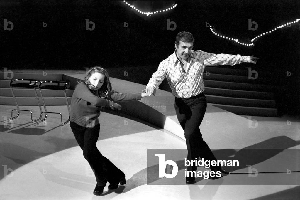 Lena Zavaroni in the Bachelors Show. Lena Zavaroni 10 yrs old has a school lesson in the make up room at the BBC theatre London with the tutor Ellis Gilmer 25 from New Zealand. Lena Zavaroni with Champers a poodle dog in one of the scenes. The Bachelors Lena Zavaroni and director Ernest Maxin. Lena Zavaroni has fun with Bachelor John (with moustashe). A big hug for Lena from Bachelor John. February 1975