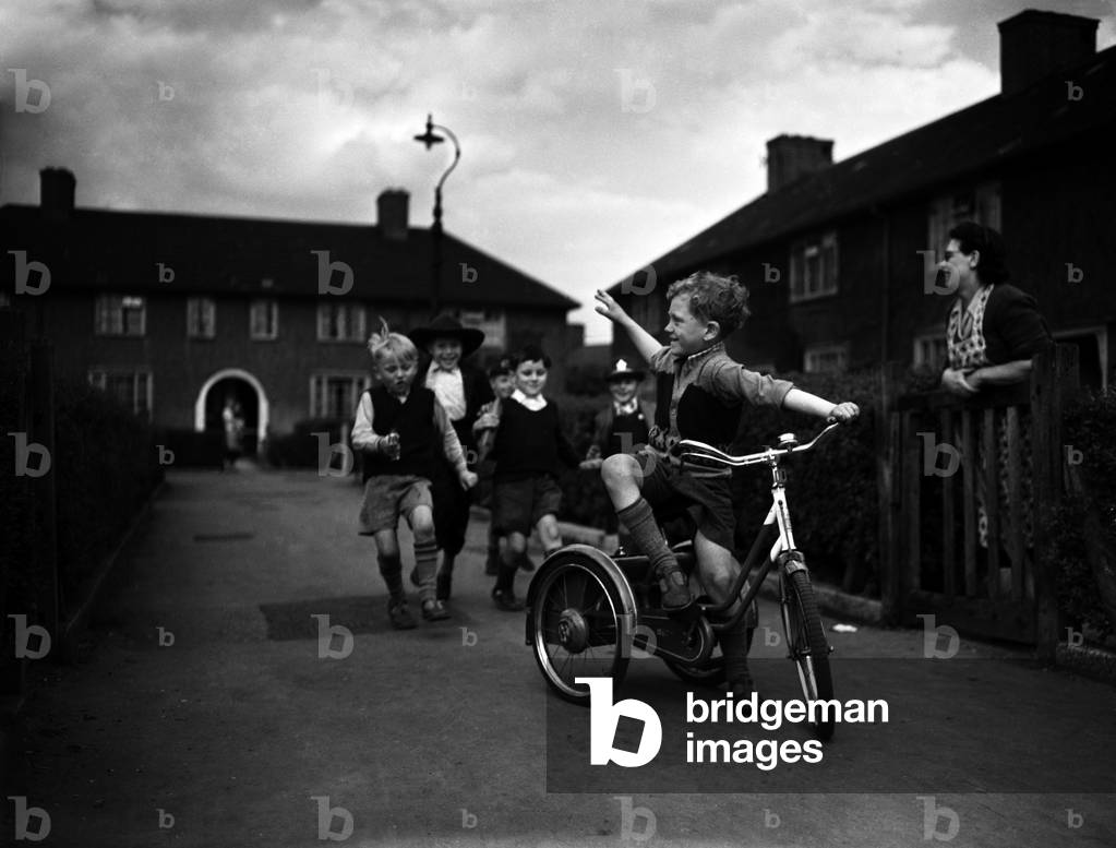 Boys playing on a council estate as one of their mothers looks on, London, 1955 (b/w photo)