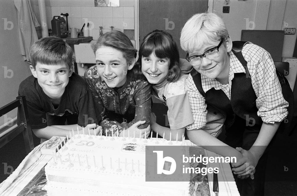 Resisting temptation... pupils of Scissett Middle School try to resist tucking into this celebratory cake, made to mark the, 50th¿niversary of the school. The four youngsters were the stars of a special production called A Trip Down Memory Lane, written by teacher Mrs Ruth Smith and produced by deputy head Mrs Judith Turner, who also made the cake. They are (from left) Philip Harrison, Sophie Mannion, Laura Kenny and Richard Brookes. The school held an open week in which visitors, who have had any connections with the school over the past, 50 years, were invited to look around. The was a display of memorabilia dating back to 1940 when the school was opened as Skelmanthorpe Modern. It change to Scissett Middle School in 1974. Today was a 1940s day when the children and staff wore clothes of that period., 10th October 1990 (b/w photo)