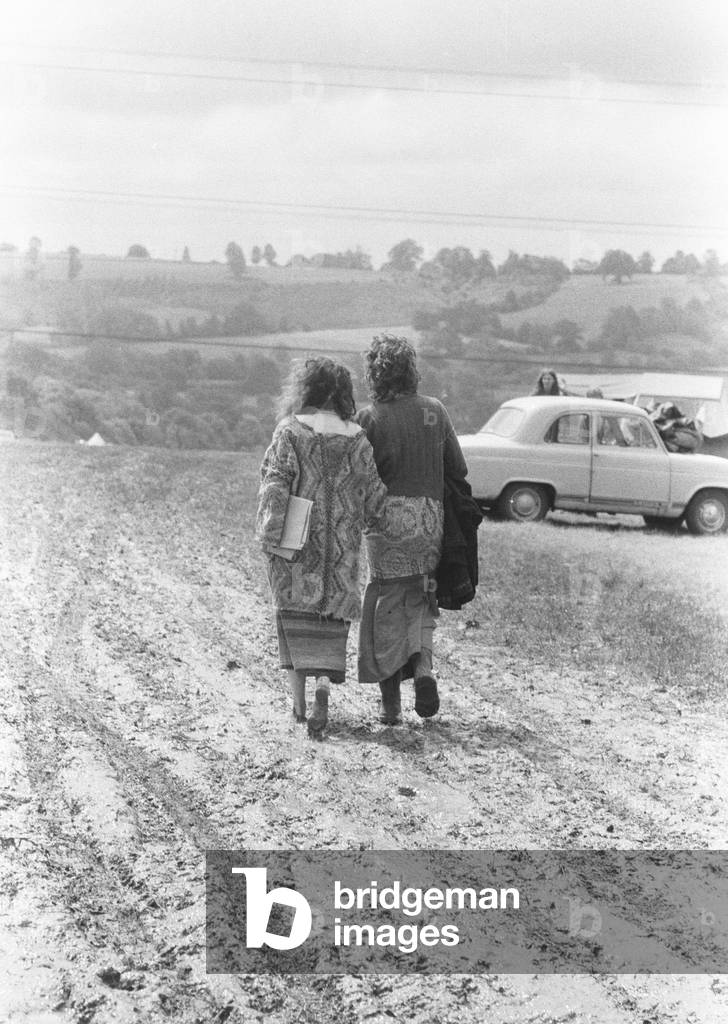 The Glastonbury Fayre of 1971, a free festival planned by Andrew Kerr and Arabella Churchill . Picture shows: Bare footed hippie couple walking through muddy fields at the festival. 19th June 1971 (b/w photo)