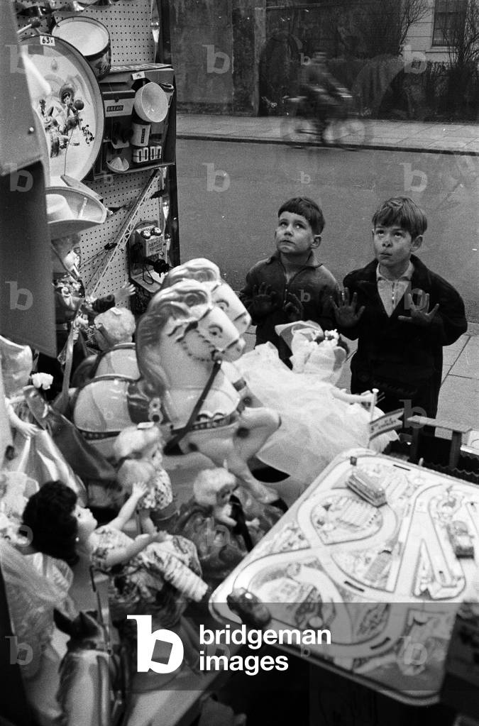 Children look longingly at toys into shop window at Christmas, 16th December 1960 (b/w photo)