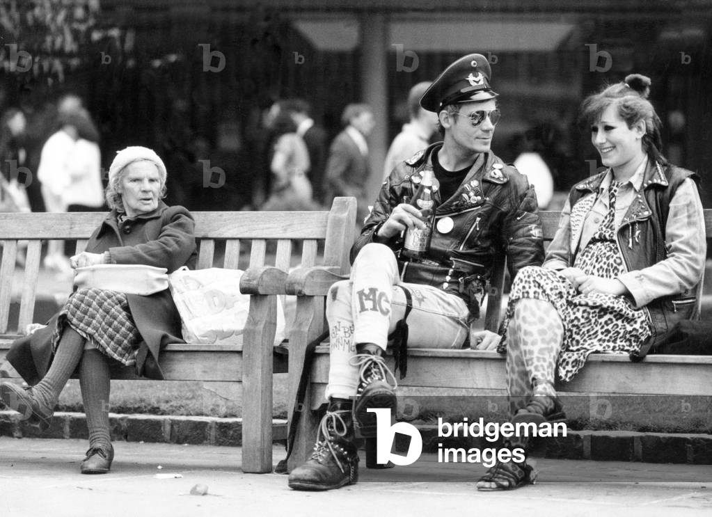 Two punk rockers sitting on a bench in Birmingham, seated next to them is an elderly lady. 28th April 1987 (b/w photo)