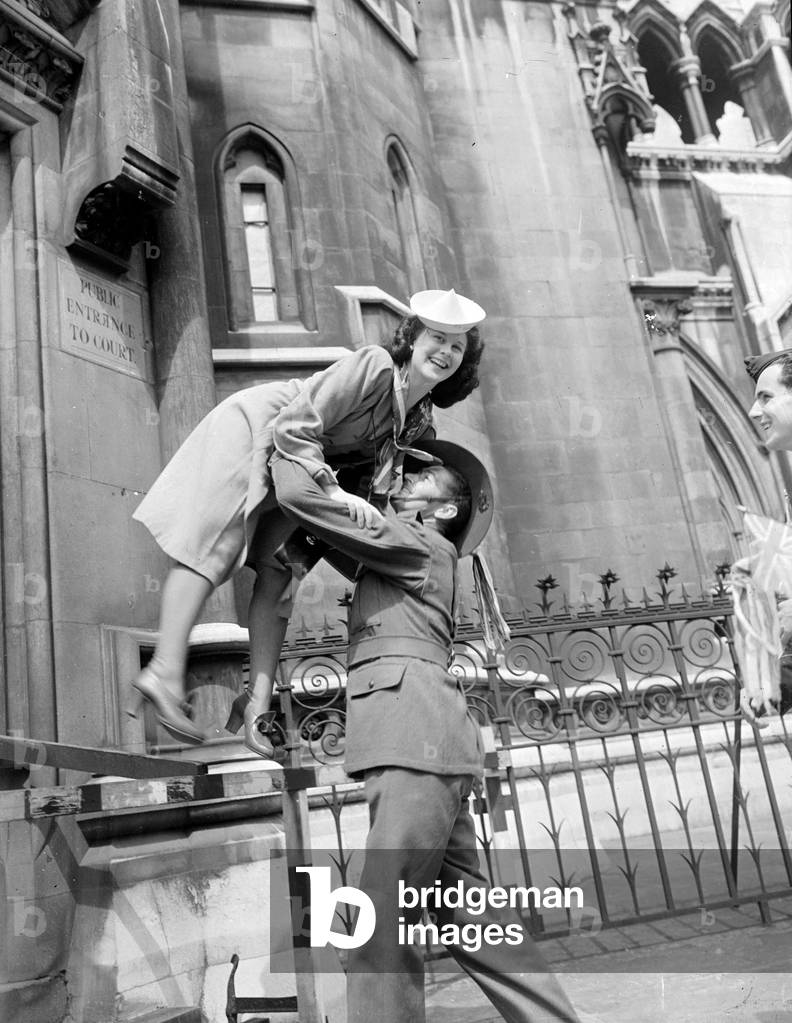 An Australian soldier helping a young lady down from her vantage point outside the Law Courts, May 1945 (b/w photo)