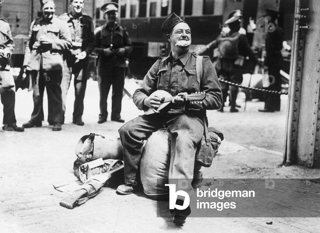 Cornishman Cecil Collins playing a banjo and eating a Cornish pasty while awaiting orders, Evacuation of British Expeditionary Force from Dunkirk, Northern France in 1940
