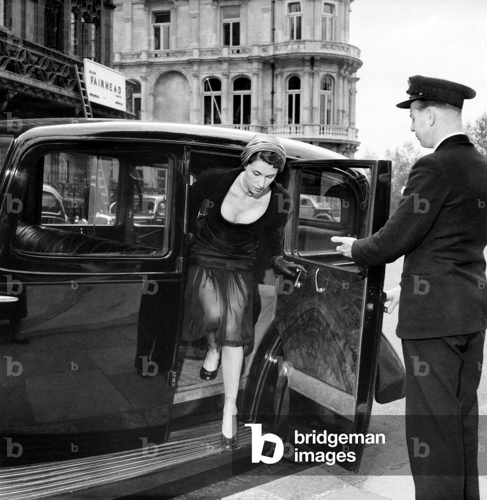 Model Jo Bevan wearing fashions of the day. being helped out from a car by a doorman. July 1952 C3529
