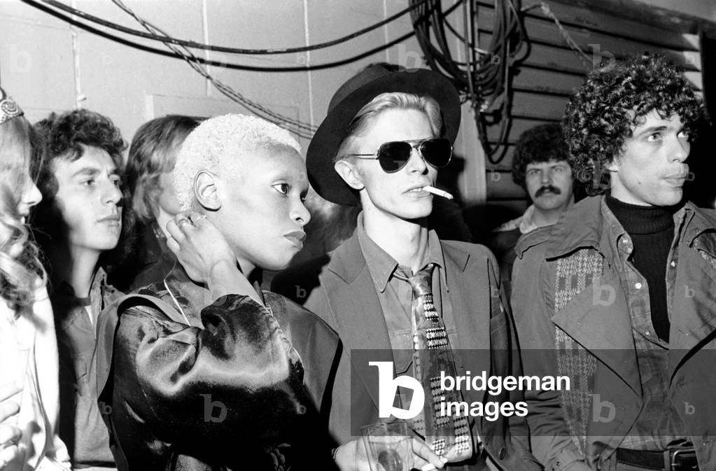 The Faces tour of the USA and Canada, February and March 1975. Kenney Jones and Gary Glitter having a drink with a woman, March 1975 (b/w photo)