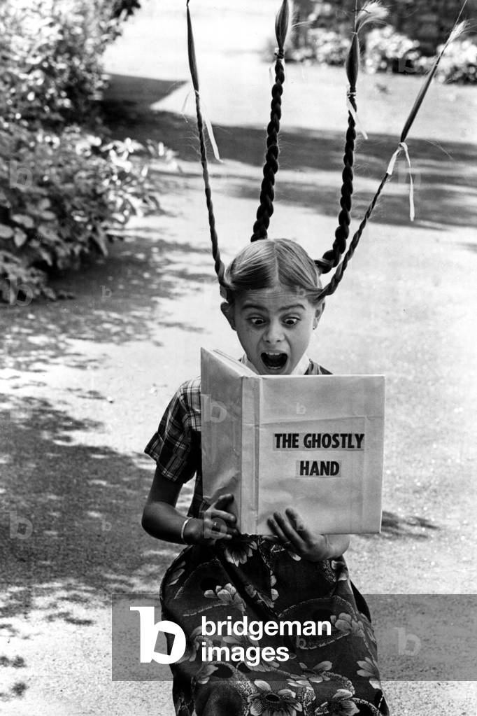 A picture from a series of humurous novelty images taken by Sunday People photographer Dennis Hutchinson. A childhood picture of journalist Lisa Hutchinson, Lisa gets a fright reading a ghost story, c. 1975 (b/w photo)