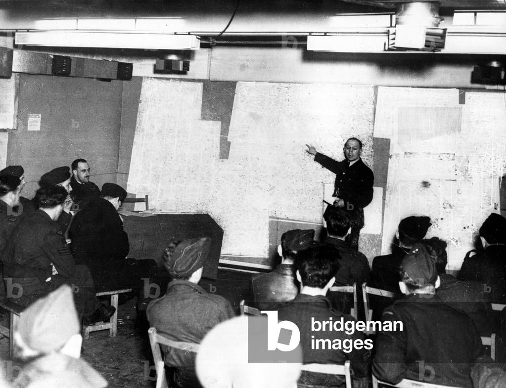Apart from its many other activities, the RAF continues to drop leaflets on Germany and occupied Europe. Picture shows crews listening to the commanding officer planning for a leaflet raid during World War Two, 27/07/1944 (b/w photo)