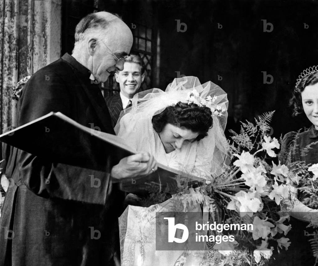 This bride forgot to sign the register. The Rector, Canon Whytehead hurried after the newlyweds and smiles as he holds the register for Mrs. Deal to sign outside St. Margaret's Church, Lowestoft yesterday. 
March 1943