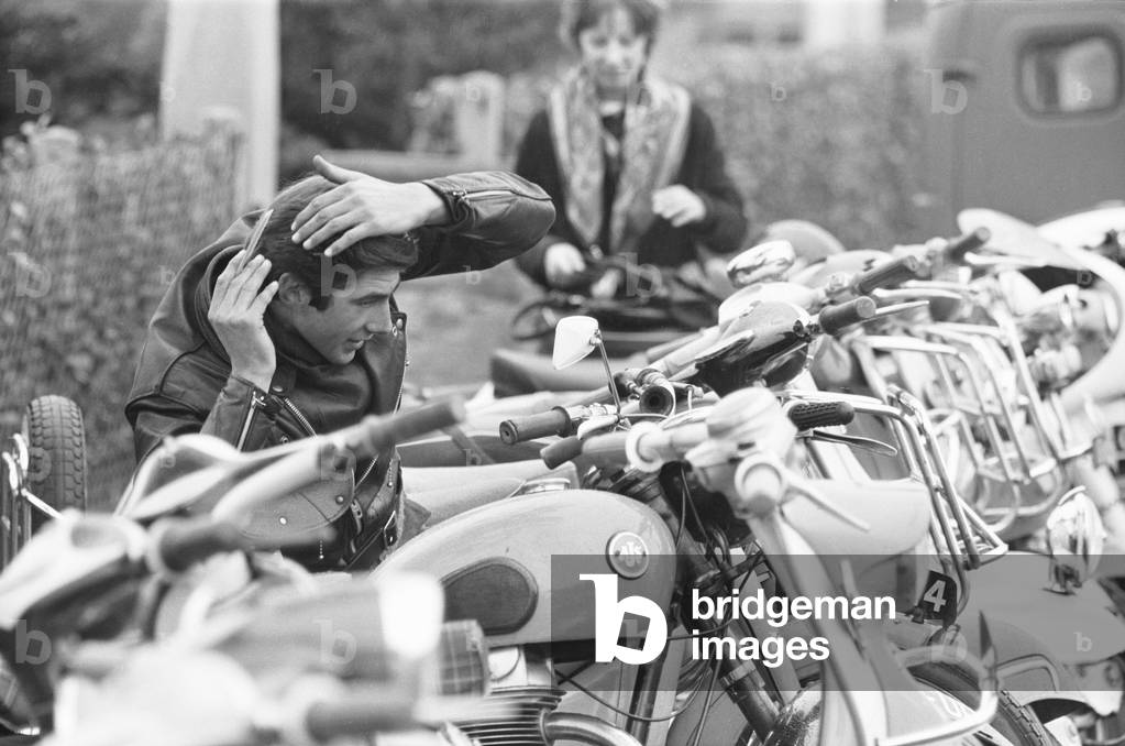 Rocker combs his hair using the mirror of a mods scooter on Clacton sea front. Over the 1964 Easter weekend several scuffles between Mods and Rockers broke out in the Essex seaside town. 30th March 1964 (b/w photo)