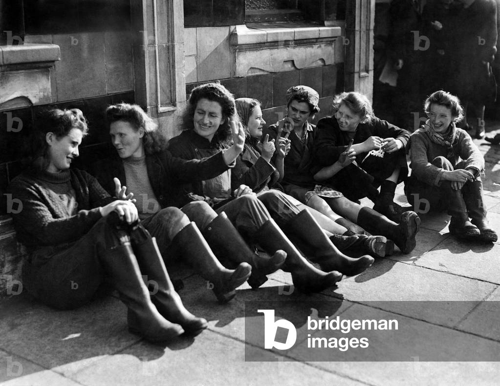 As herring catches have not come up to expectation these English, Irish and Scottish fisher girls spin yarns on the fish wharf whilst waiting for herring supplies. 
December 1945
