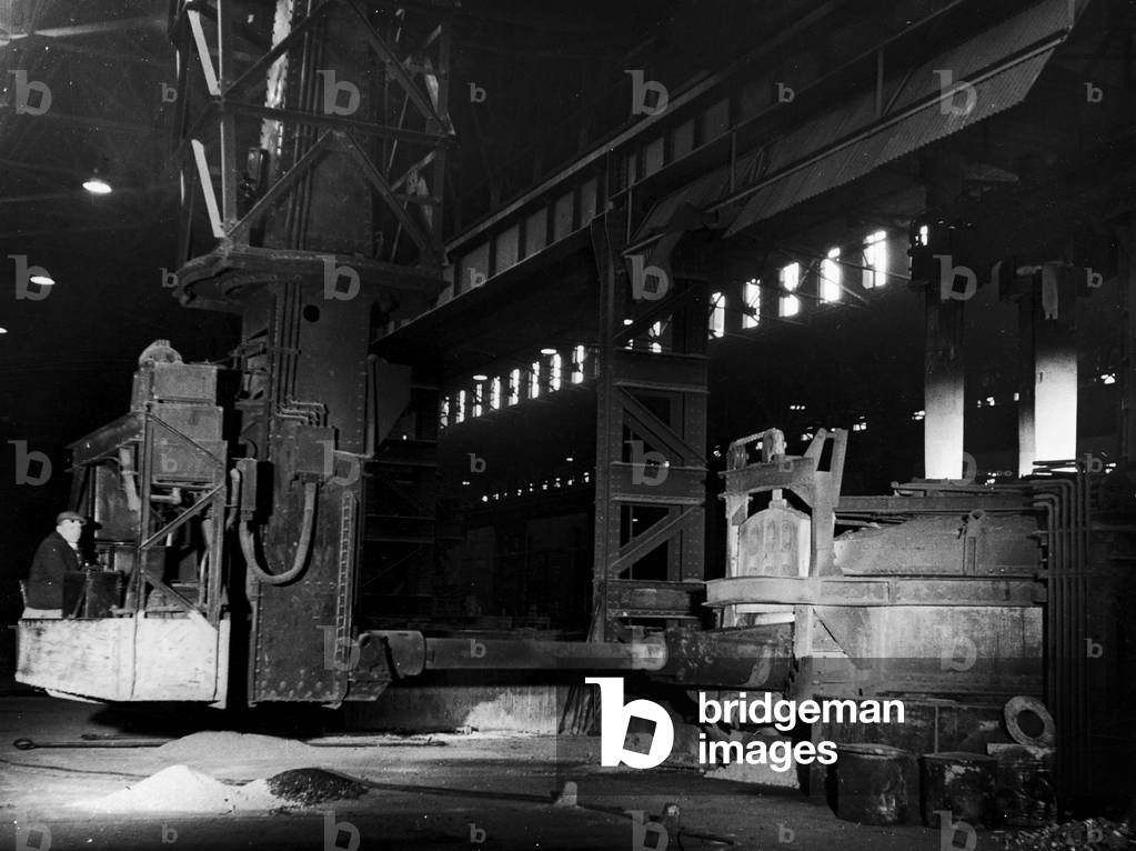 A mechanical charging machine feeding a 30 ton electric arc furnace at the English Steel Corporation Works (Vickers) in Sheffield, which specialises in the electrical induction method. The raw material used to charge the furnace - scrap metal, alloy etc, is weighed out into special steel pans. A charger arm (or 