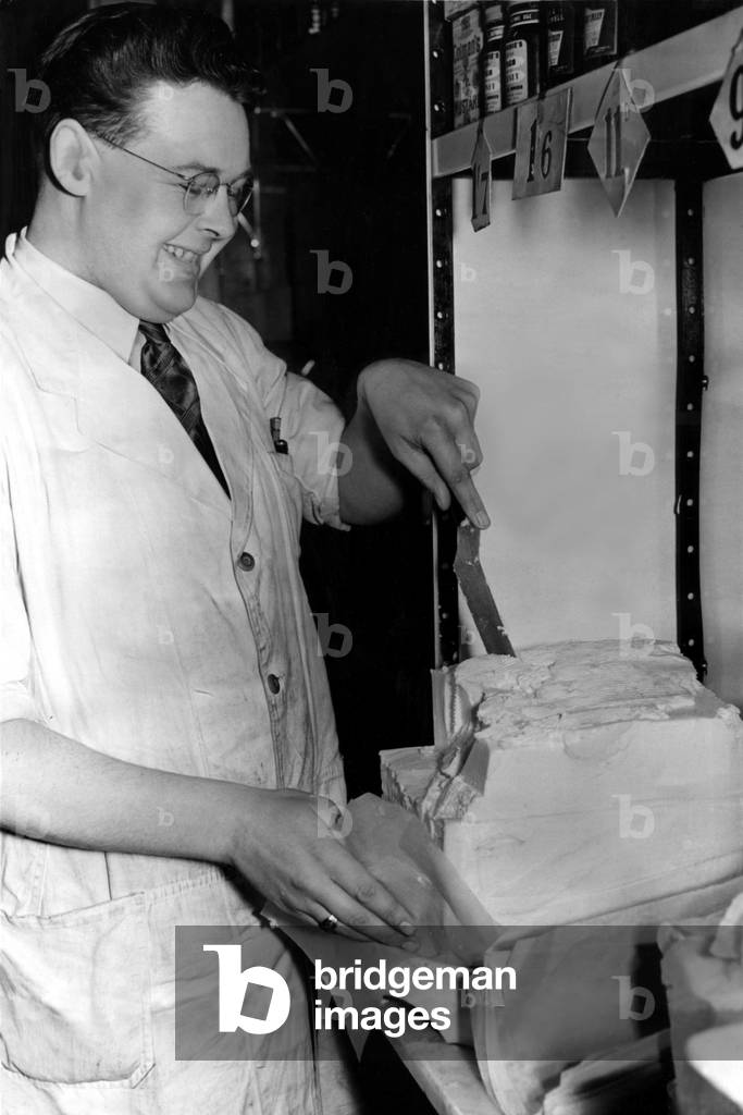 Post World War Two - Second World War - City grocery assistant, Mr William Wanup, makes a 'celebration cut' on the first day of derationing of butter, 14 years after rationing of it began. 10th May 1954 (b/w photo)