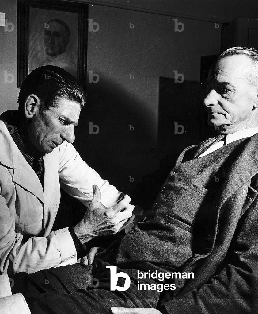 Dr Robert injects a hypodermic into his patient suffering from a gastric ulcer., c.1955 (b/w photo)