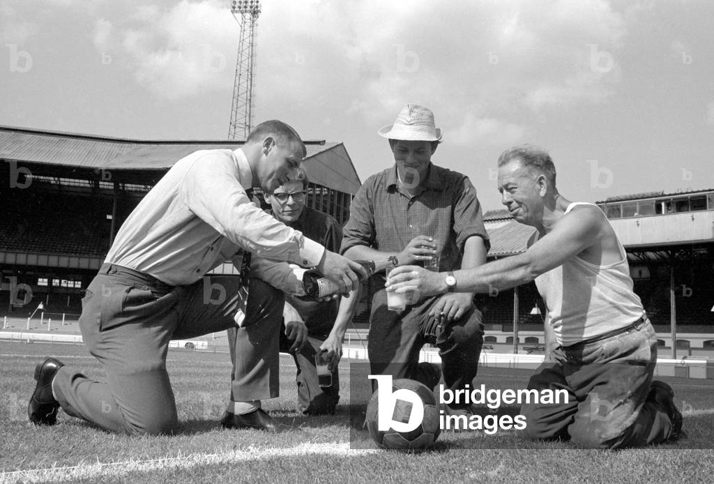 Chelsea manager Tommy Docherty christens the centre spot of the Stamford Bridge pitch with champagne watched by groundstaff , before the start of the new season August 1965 (photo)
