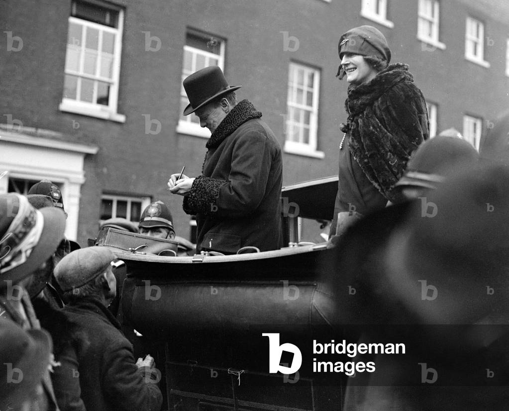 Winston Churchill is seen with his wife Clemantine Churchill in an open topped car signing his autograph for the people of Epping. October 1924 (b/w photo)