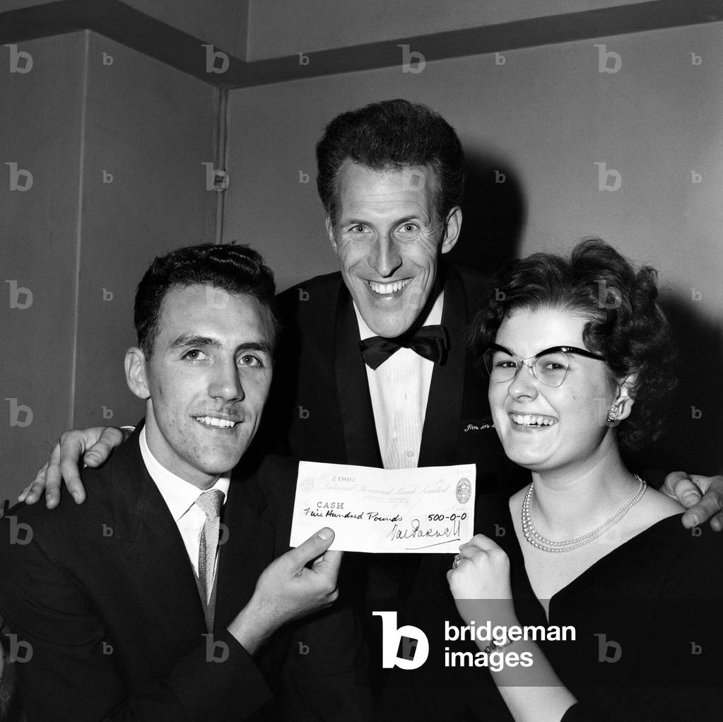 Mr and Mrs Farquhar who have only been married for 24 hours, won £500 on the Sunday Night at the Palladium game show, Beat the Clock. Pictured are Mr and Mrs Farquhar with the cheque and compere Bruce Forsyth in the middle. 11th October 1959 (b/w photo)