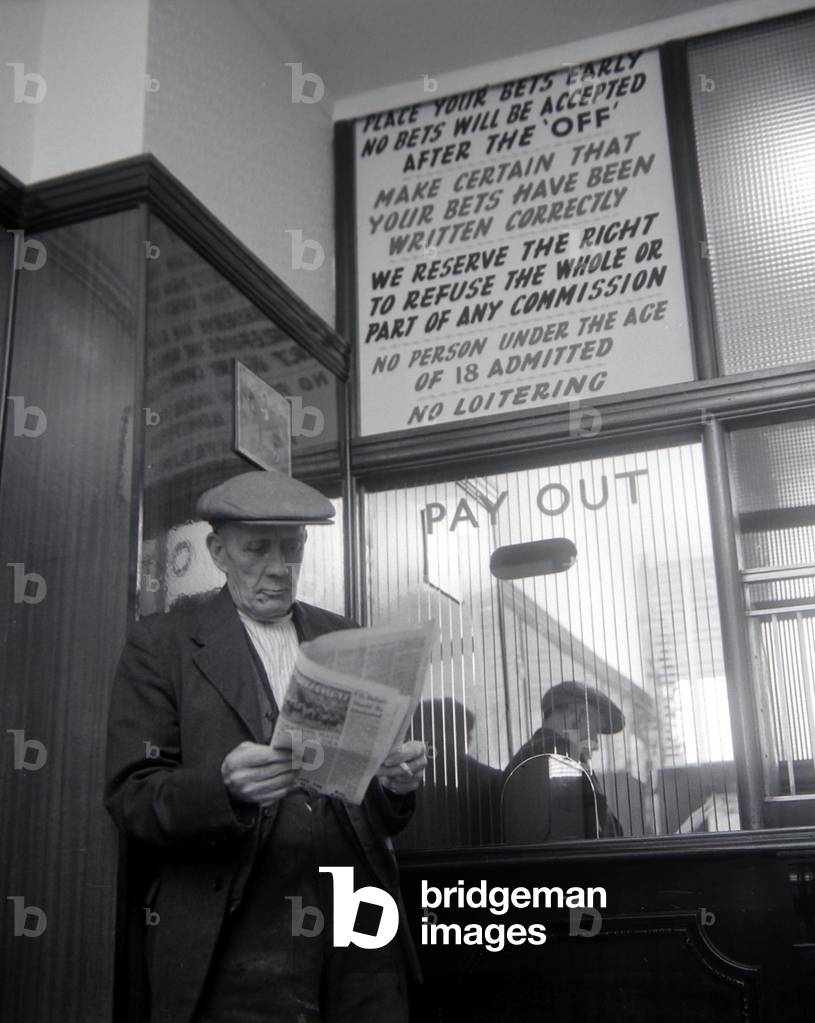 An elderly man studies the form guide inside A E Fane and Co betting shop in Islington, London before placing his bet
May 1961