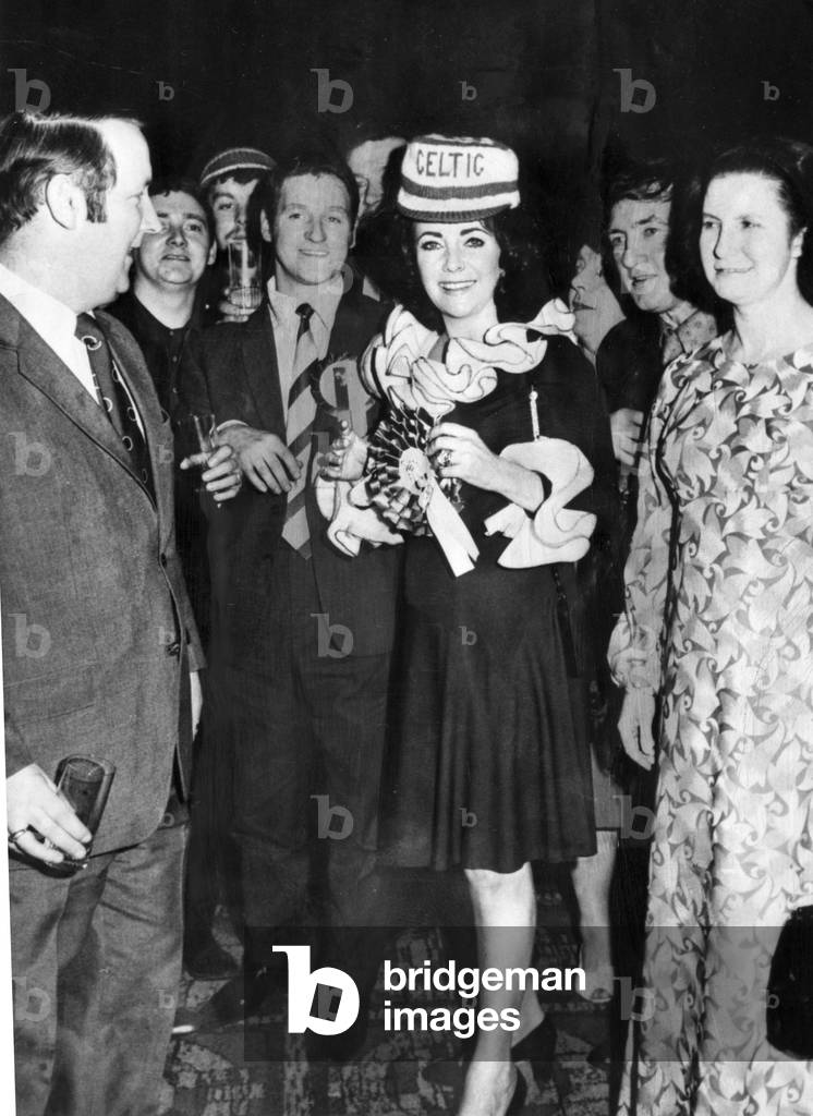 Film actress Elizabeth Taylor, made an honorary Celtic fan after flinging a £5000 victory party with her husband Richard Burton, for the Scots following their victory over Ujpest Dozsa in a European Cup tie. Taylor is pictured wearing a Celtic hat. 10th March 1972 (b/w photo)