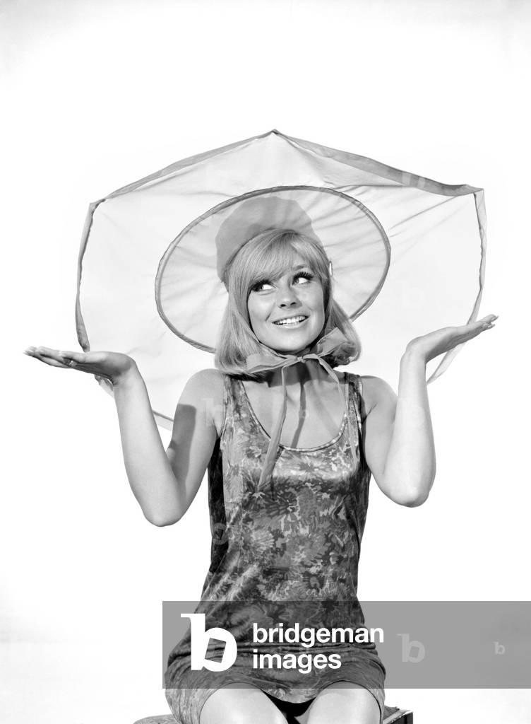 Clothing: Fashion: Hats: Woman wearing umbrella hat. Model: Marilyn Rickard. 1966 (b/w photo)