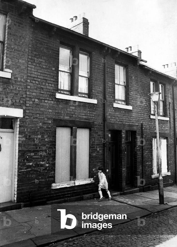 A boarded up house in Kirk Street, Byker, Newcastle, in which a man died on the 25th May, 1974. A girl is pictured walking / running on the pavement, 26th May, 1974 (b/w photo)