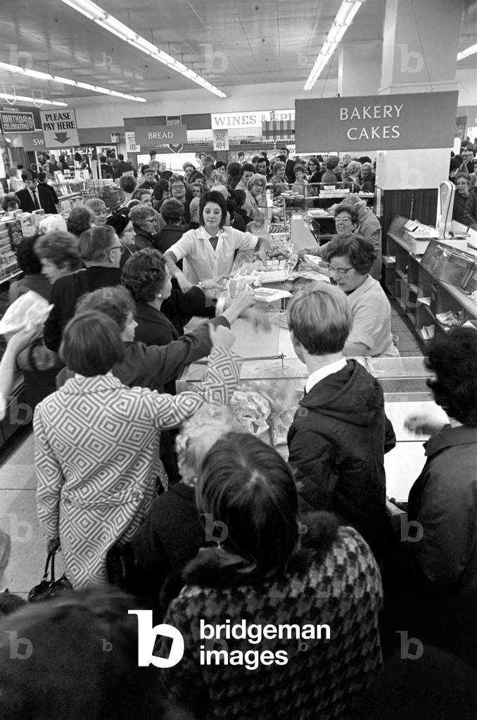 Scores of shoppers line the counter at Lewis's store in Manchester, waiting for a delivery of bread to fill the empty shelves, during a bakers strike in the North West of England, October 1969 (b/w photo)