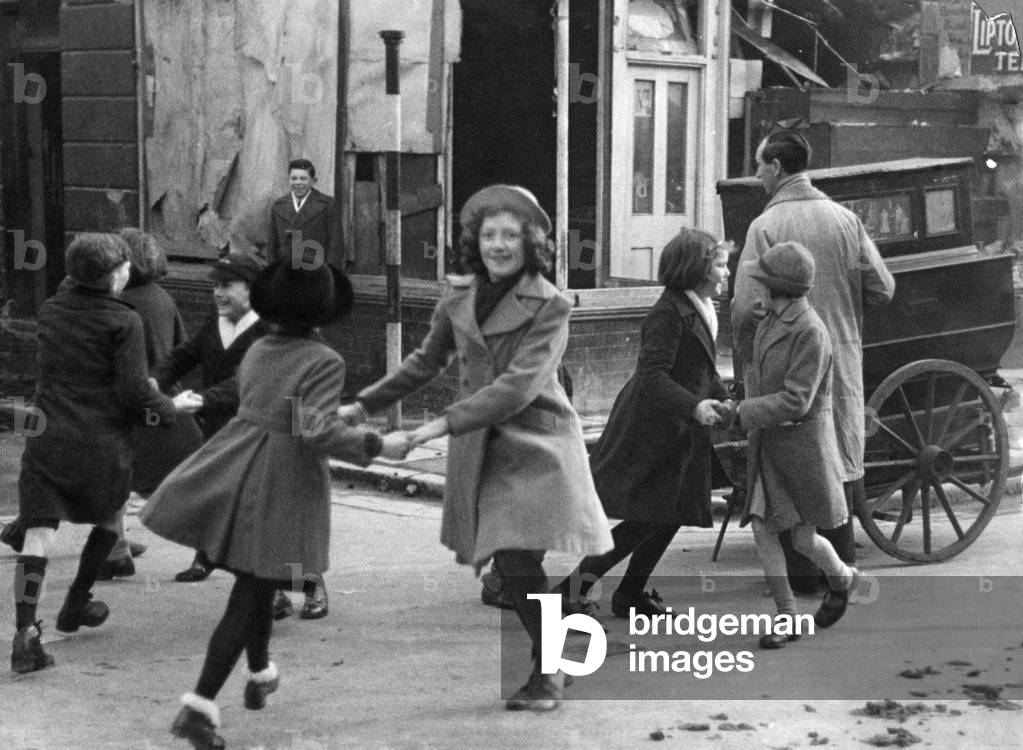 Children dance to the sound of a barrel organ in one of London's bombed streets, 5th February 1941 (b/w photo)