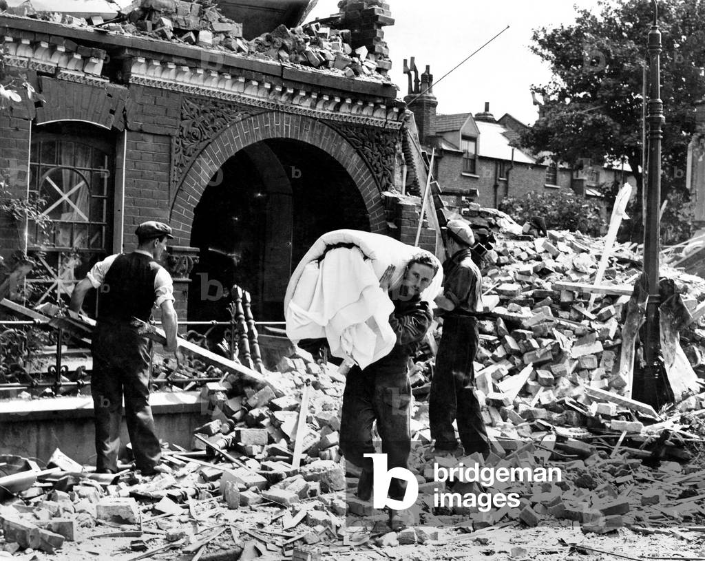 Corporal I.C. Davis came home on leave last night to his London home and here he is seen salvaging bedding from his wrecked home in Trinity Road, Tooting. 
1944
