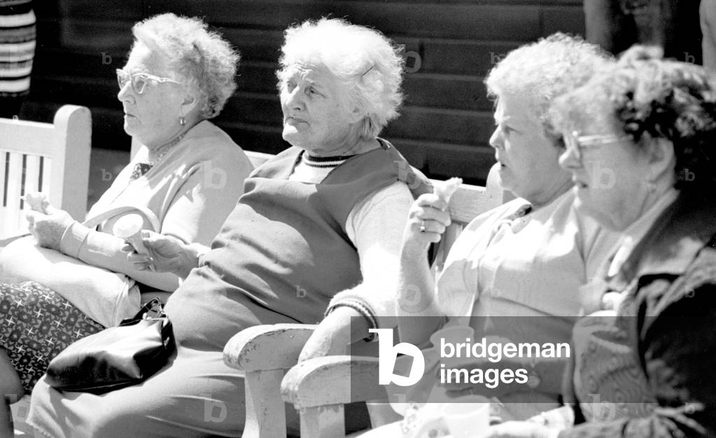 Old ladies sitting on a bench eating ice cream during a day out to the beach at Trecco Bay, South Wales. 6th August 1977 (b/w photo)