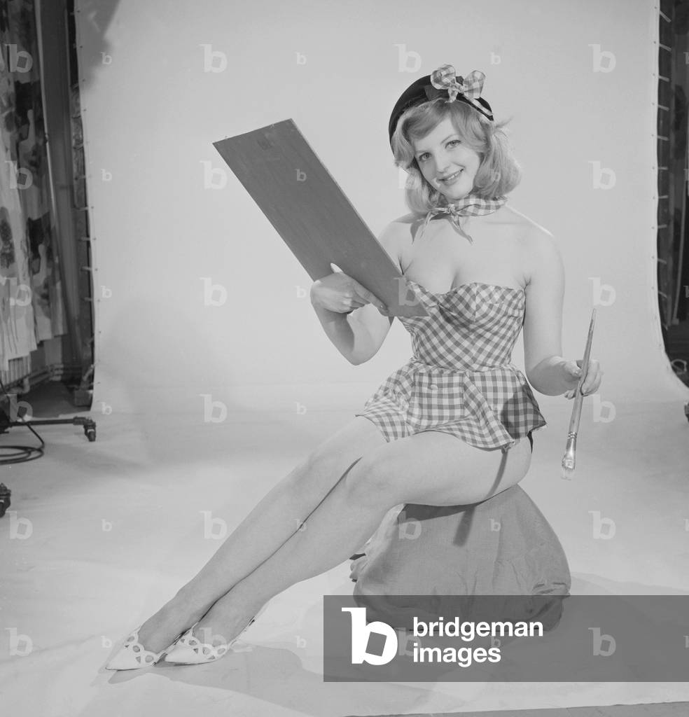 Reveille art Feature, Model Peggy Cage seen here wearing a check short summer dress holding a palette and brush, c.1960 (b/w photo)