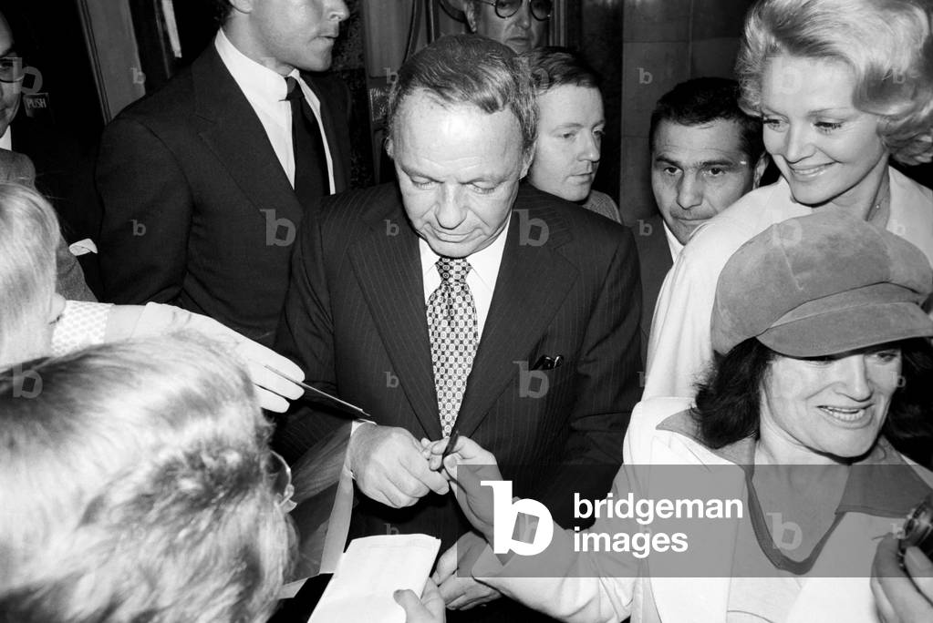 Frank Sintara and his girlfriend Barbara Marx leaving Claridge's on the way to Mirabellas restaurant in Curzon St Frank stopped outside the hotel to sign autographs for a few waiting fans, May 1975 (b/w photo)