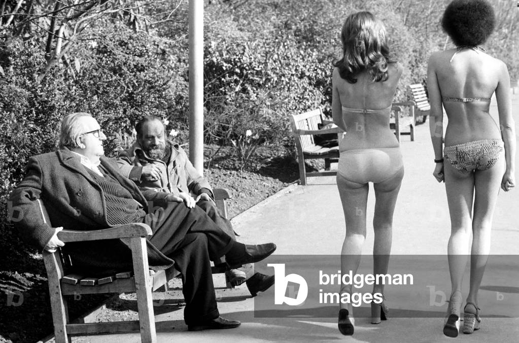 Fashion scene from Woolworth's. Two old men sitting on a park bench distracted by models in bikini walking past
February 1975