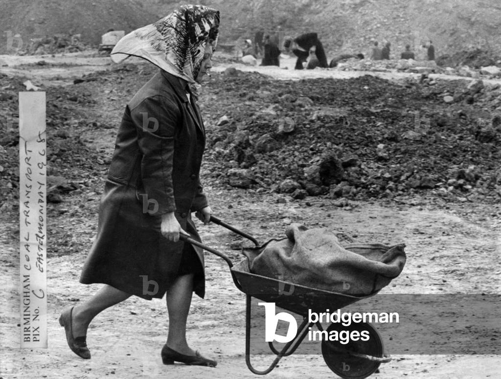Woman wheeling a wheelbarrow filled with a sack of coal at Bentley Lane in Walsall, Staffordshire.