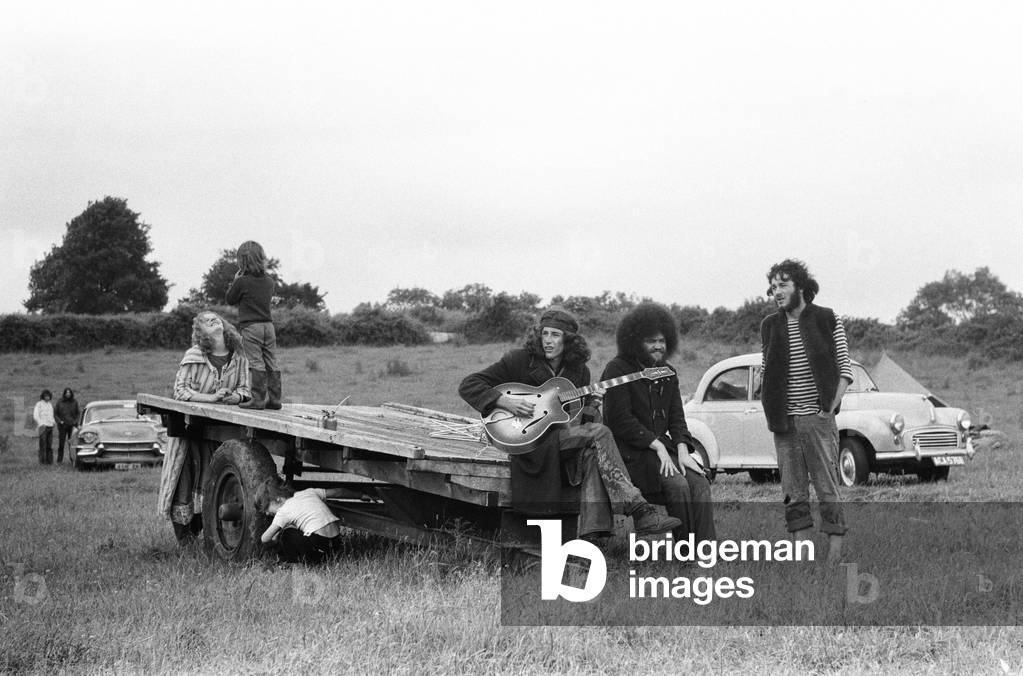 The Glastonbury Fayre of 1971, a free festival planned by Andrew Kerr and Arabella Churchill . Picture shows: Group of friends sitting on the back of a trailer playing guitar and singing songs at the festival. 19th June 1971 (b/w photo)