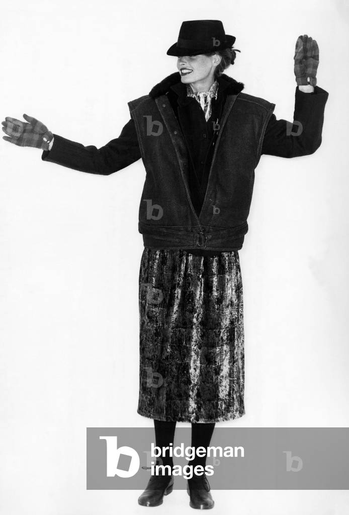 Fashion - 1970s. From Aldo Ferrante comes a square-shouldered sheepskin waistcoat with a navy blue blazer, panne velvet scarf, hat and plaid gloves. April 1978