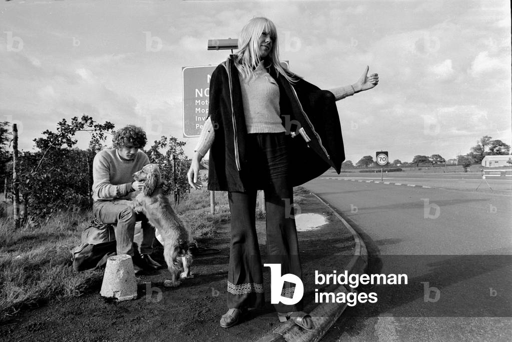 A young couple and their dog trying to hitch hike and get a lift on the motorway September 1970 (b/w photo)