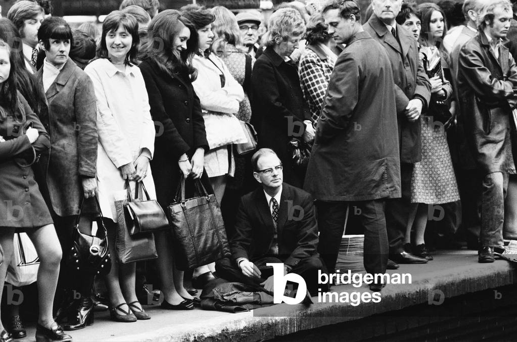 One man decides to sit down on the platform as homeward bound crowds await their train during rush hour at Liverpool Street Station, London. 18th April 1972 (b/w photo)