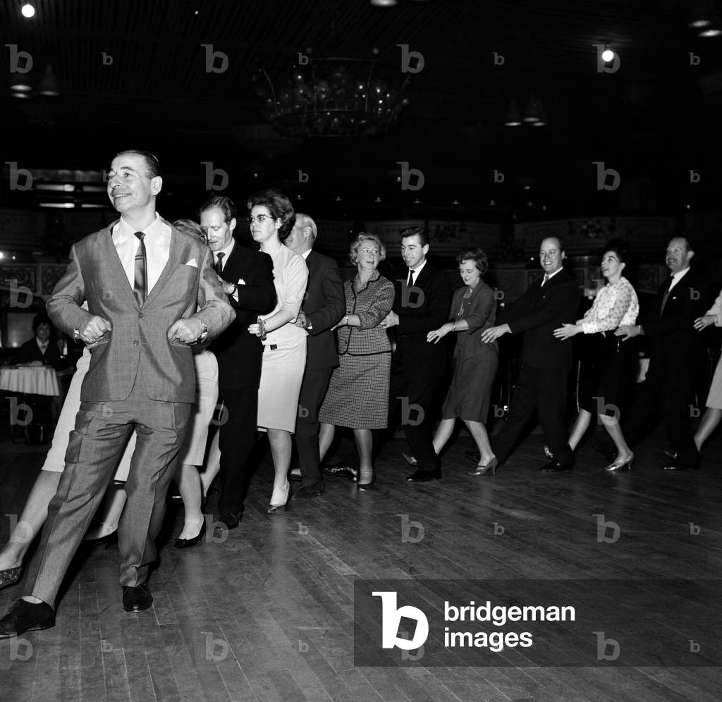 Band leader Joe Loss introduced a new party dance at the Hammersmith Palais called the Finnjenka. Here he demonstrates the dance leading the dancers into the streets and back in to the dance hall. 22nd October 1964 (b/w photo)
