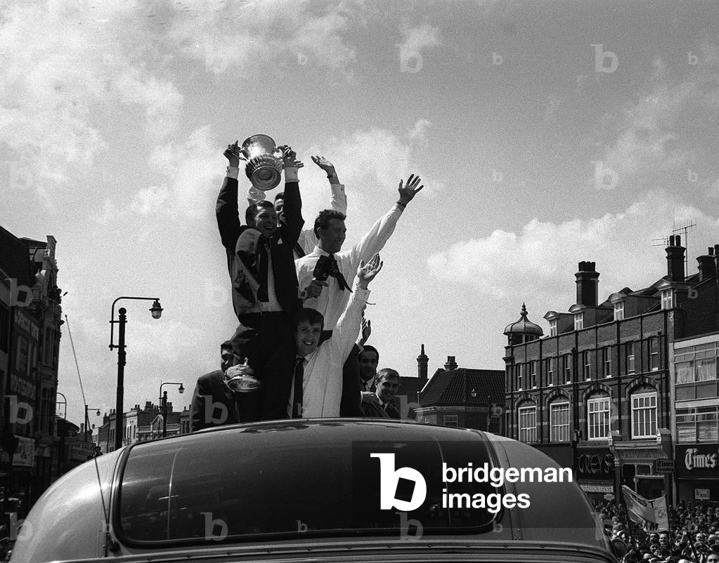 Bobby Moore holds up the FA Cup during the parade around East London after the Hammers had won the FA Cup in 1964Holding him safe is full back John Bond (photo)